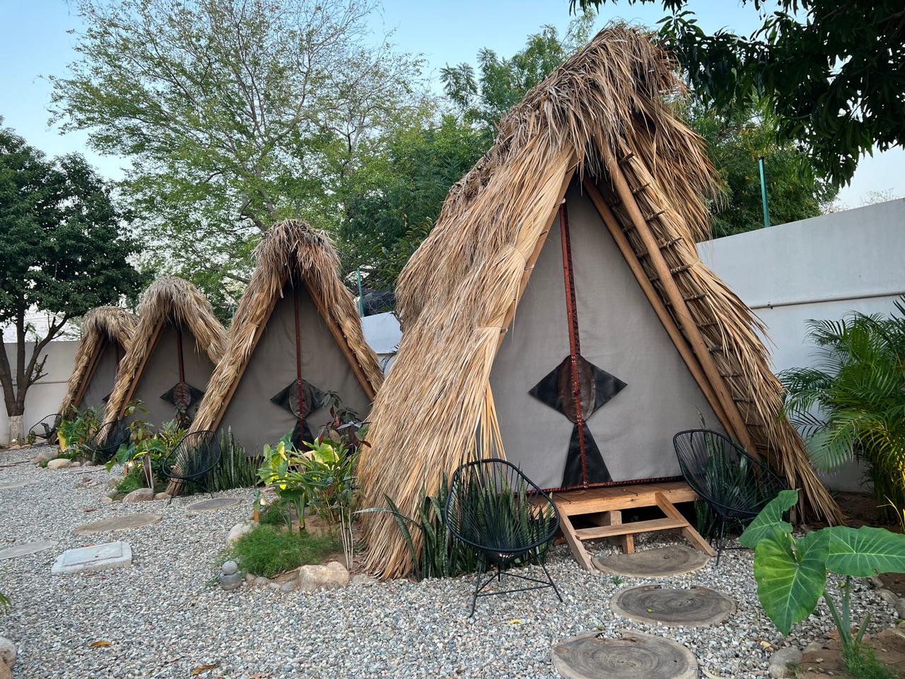Teepees de palma de Tribu Glamping & Surf entre jardines