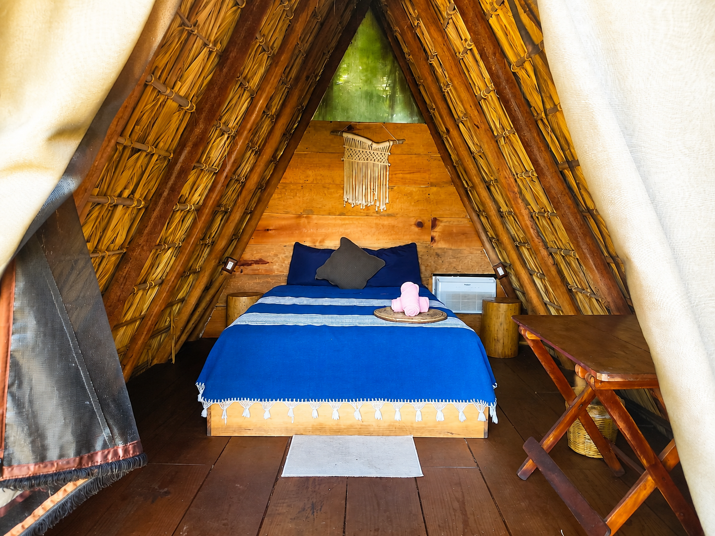 Cama de matrimonio bajo techo de palma en interior de teepee